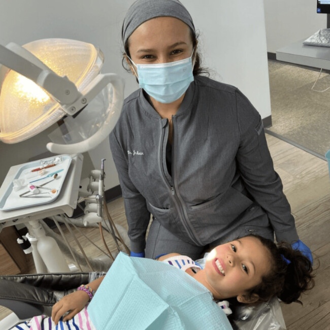 Dentist with a blue mask on behind a pediatric dental patient lying down for dental cleaning