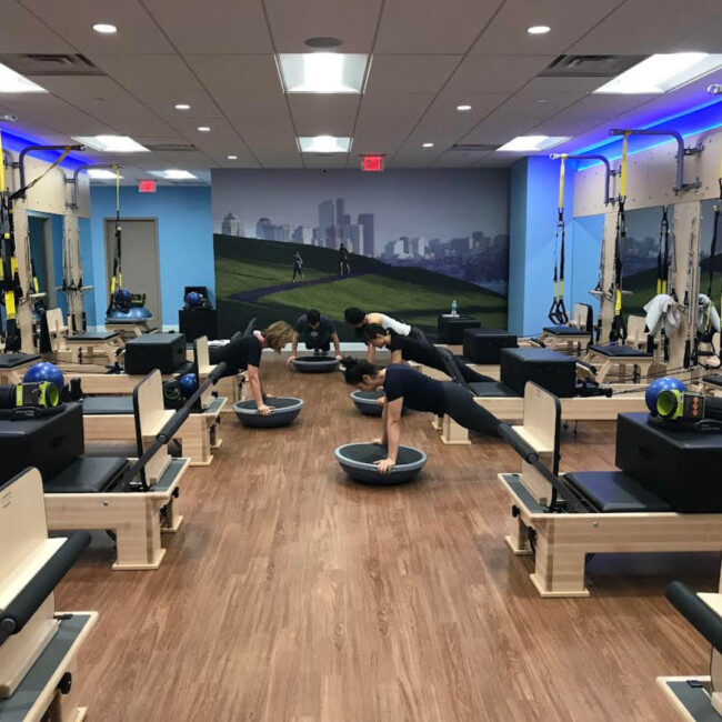 Club Pilates studio with reformers and Pilates class participants using half-balls for planks