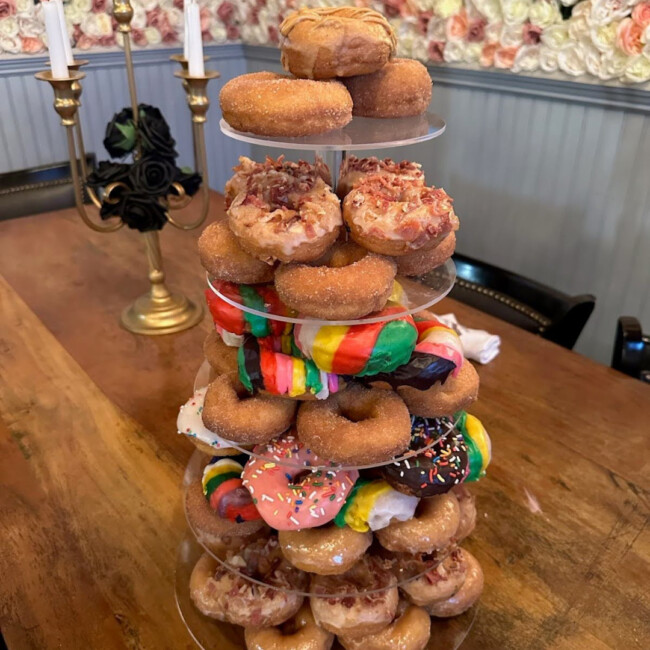 A tower of doughnuts with tiers of colorful glazed and plain doughnuts sits on a table