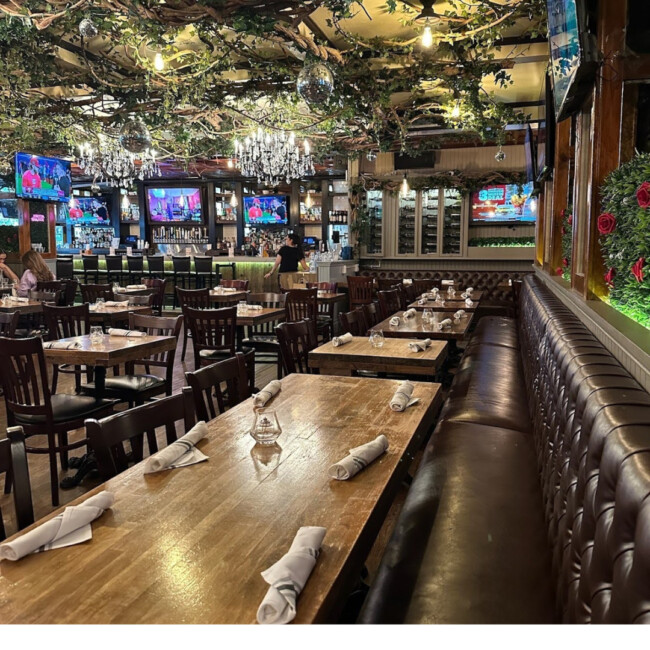 Interior view of The Ainsworth with greenery on the ceiling and long tables with booths and chairs