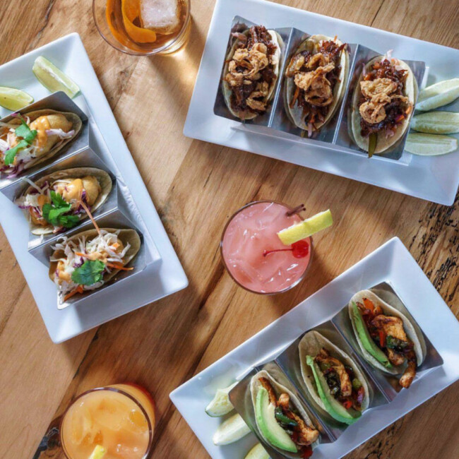 Overhead view of a table with plates of tacos and cocktails at the Ainsworth