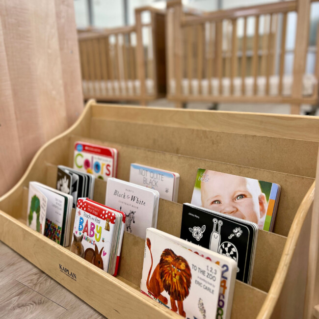 Wood cribs in background and wood book shelf with nine board books