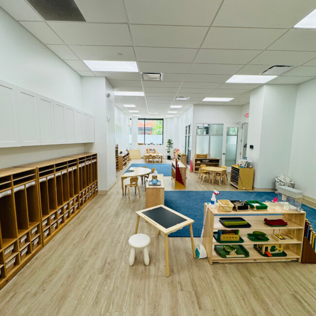 Classroom view with wood cubbies, blue rug, wood shelves, and toys