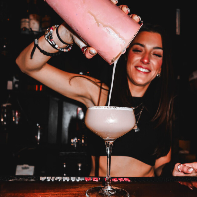 Bartender pouring a pink drink from a shaker into a glass