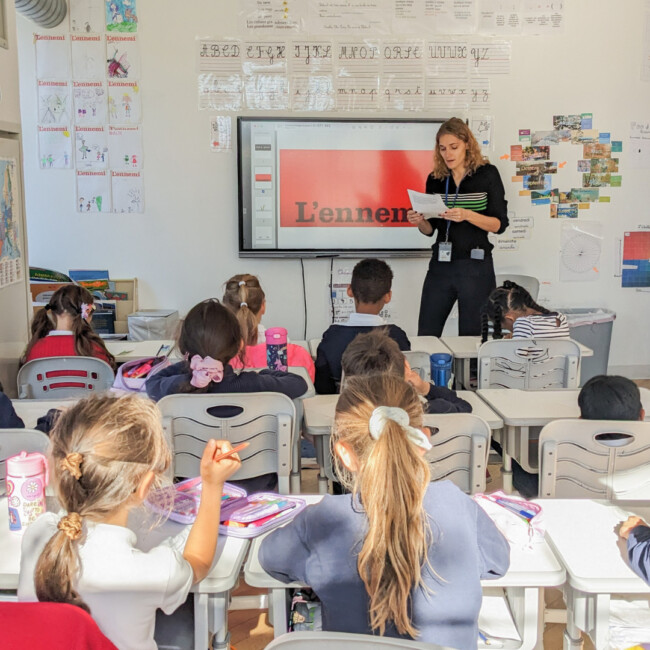 Teacher standing in front of a classroom reading a piece of paper