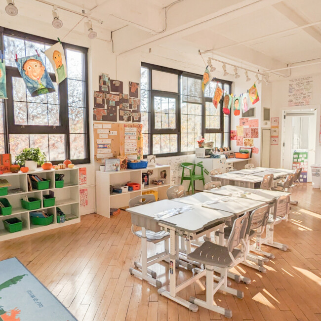 Empty classroom with table, chairs, large windows, and art hanging from the ceiling