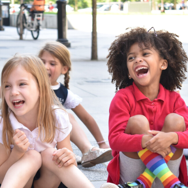 Three students sitting on the ground laughing