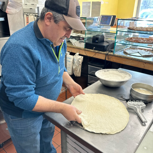 Man wearing blue sweater and hat making pizza